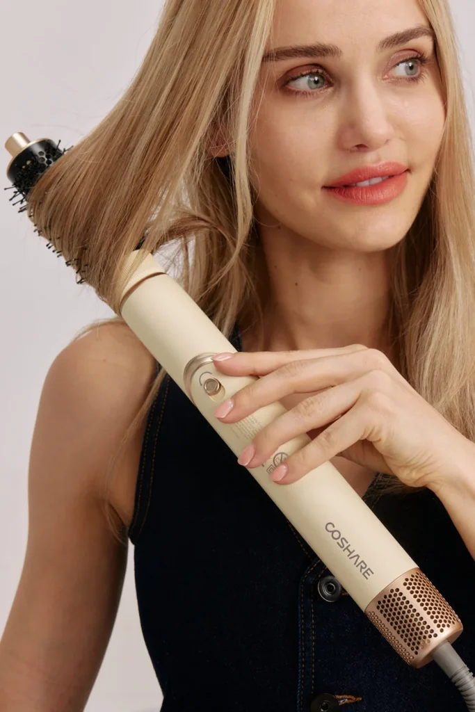 Kobieta z długimi blond włosami układa je suszarko-lokówką COSHARE InStyle 4w1 z okrągłą szczotką