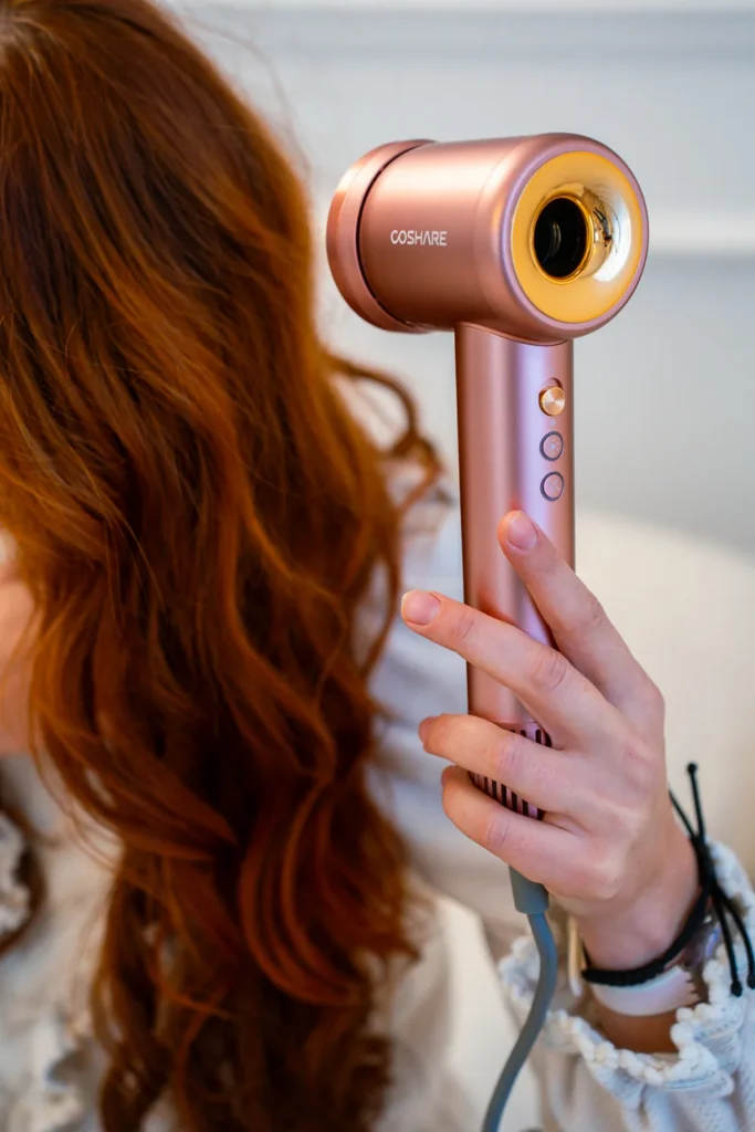 Suszarka do włosów COSHARE SuperFlow1 Standard Rose Gold w dłoni podczas suszenia długich rudych włosów